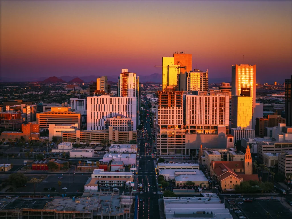City skyline at sunset with tall buildings reflecting orange light and distant mountains